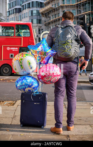 L'homme vu de dos, roulant une valise avec 40e anniversaire ballons attachés à gérer Banque D'Images
