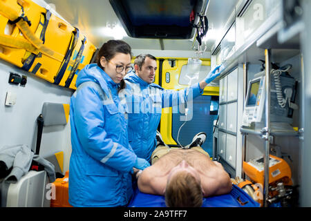 L'examen paramédical homme malade sur civière, tandis que son collègue de la préparation compte-gouttes Banque D'Images