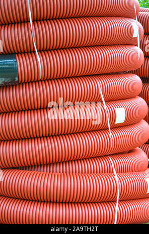 De nouvelles bobines de tuyau en plastique rouge avec des gouttes de pluie. Le tube en plastique rouge pour la protection du câble souterrain. Premier étage d'une pelote de tube ondulé rouge. Pla Banque D'Images