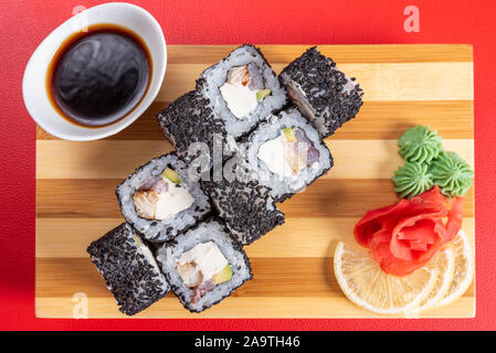 Sushi, rouleaux de sésame noir, avec du fromage, de la crevette et du crabe. Sur la planche. Sur un fond rouge. Banque D'Images