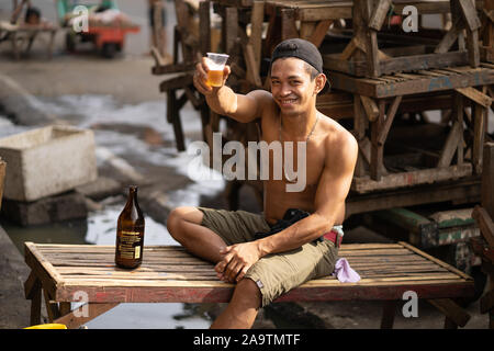 Un jeune homme de son pays souriant offre un verre de bière au photographe tôt le matin dans la zone de marché, Cebu City,Philippines Banque D'Images