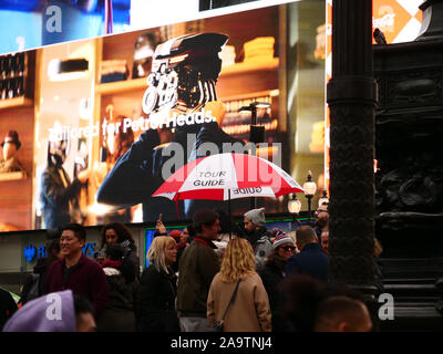 Guide touristique avec parapluie rouge et blanc vu avec un groupe de touristes à Piccadilly Circus, Londres, Angleterre, Royaume-Uni en novembre 2019. Banque D'Images