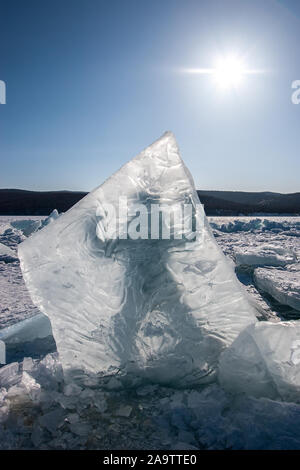 Un gros bloc de glace se tient à la verticale dans le lac Baïkal gelé et derrière elle une silhouette d'un homme. Ciel bleu avec le soleil. Châssis vertical. Banque D'Images