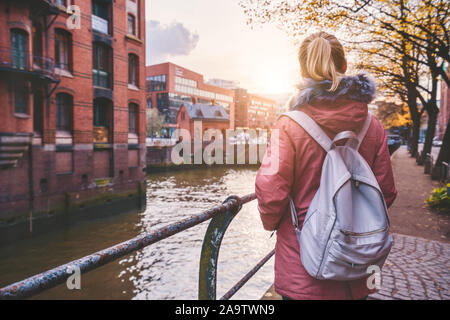 Retour Vue arrière du sac à dos femme adultes avec tourisme bénéficiant d'automne beau coucher de soleil sur la scène historique d'entrepôts Speicherstadt à Hambourg Banque D'Images