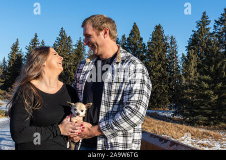 Joli jeune couple partage un moment spécial ensemble sur un pont en bois dans un parc sur un après-midi d'hiver ensoleillé. Banque D'Images