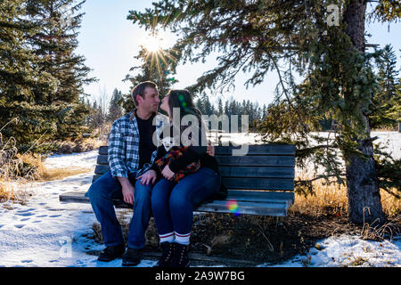 Un couple dans la trentaine, avec un chihuahua blanc, assis sur un banc de parc, de partager un moment privilégié, entouré d'arbres et un brillant sunburst. Banque D'Images