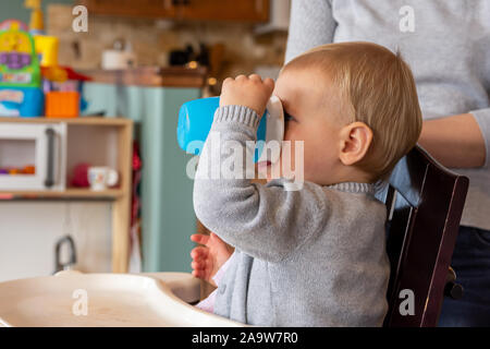 Les jeunes, bébé fille est assise dans sa chaise d'un verre de sa tasse. Banque D'Images