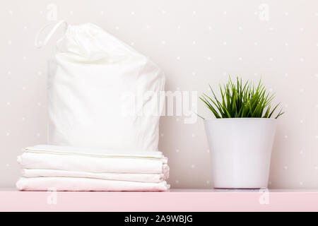 Une pile de literie propre, un sac de rangement, une usine d'accueil sur une table contre un mur de lumière. Banque D'Images