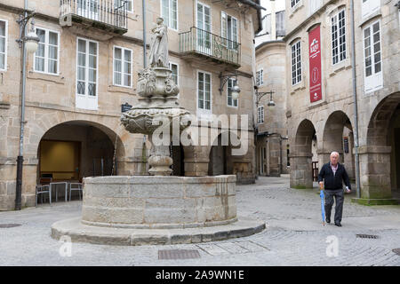 Un homme passe devant la fontaine de San Vicente Ferrer dans la Praza do Campo dans la région de Lugo, Espagne. Dans la distance est la Puerta del Obispo Odoario. L'anci Banque D'Images