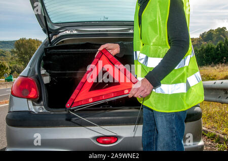 Woman getting triangle d'avertissement rouge hors de sa voiture en panne, France Banque D'Images
