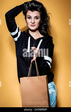 Happy brunette girl est titulaire d'un achat dans un sac d'artisanat sur fond orange. Banque D'Images