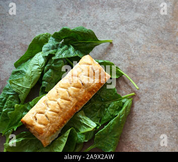 Mise à plat d'un rouleau de saucisse sur un lit de feuilles de salade verte sur un fond brun clair avec l'espace blanc Banque D'Images