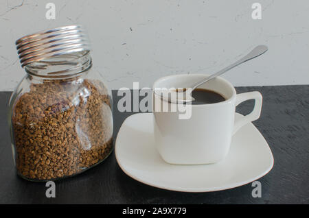 Un bocal de verre de café instantané en granules à côté d'une grande tasse blanche. Banque D'Images