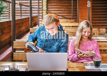 Jeune mec joue à des jeux sur un ordinateur portable dans un café à proximité. La jeune fille est en train de lire un livre. concept d'usure Banque D'Images