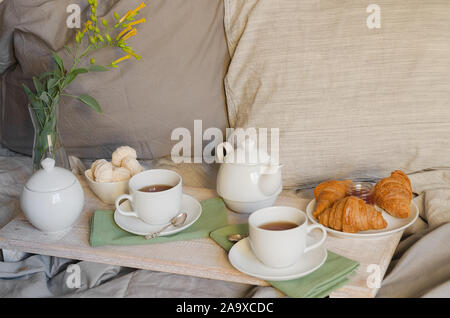 Détendre le petit déjeuner au lit. Théière et deux tasses, de croissants et de meringue sur le plateau avec des fleurs. Style scandinave. Banque D'Images