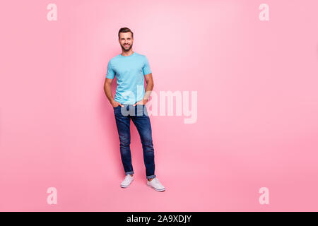 Toute la longueur de la taille du corps photo de cheerful confiant guy tenant les mains dans les poches de jeans vêtus de blanc fond couleur pastel isolées chaussures Banque D'Images