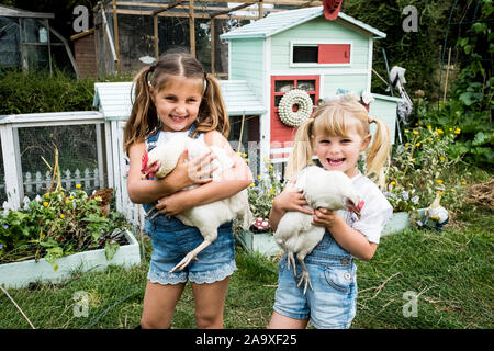 Deux filles debout en face de poulailler dans un jardin, holding white poulets, smiling at camera. Banque D'Images