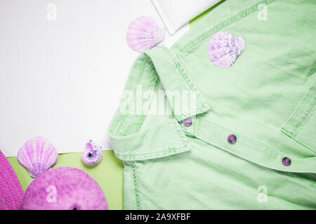 Vue de dessus de la maison de l'habillement et accessoires d'été. Chemise en jean, les coquillages sur fond vert, papier blanc vierge pour le texte. Fashion blogger, s Banque D'Images