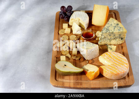 De nombreuses sortes de fromages servi sur planche de bois avec des noix, raisins sur fond clair. Copy space Banque D'Images