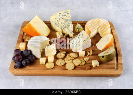 De nombreuses sortes de fromages servi sur planche de bois avec des noix, raisins sur fond clair. Close up Banque D'Images