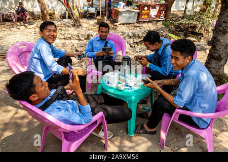 Un groupe de jeunes hommes birmans assis autour d'une table à la recherche de leurs téléphones portables, Mandalay, Myanmar. Banque D'Images
