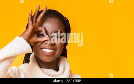 Portrait d'afro girl positive couvrant les yeux à geste okay Banque D'Images