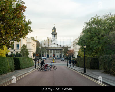 Cyclistes traversant York Gate Street près de Regents Park avec l'église paroissiale St Mary derrière, Marylebone, Londres. Banque D'Images