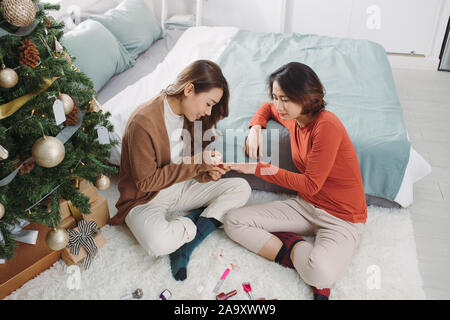 Deux jeunes amies du polissage des ongles dans la salle de séjour à la maison pendant les vacances. Le temps de Noël. Banque D'Images