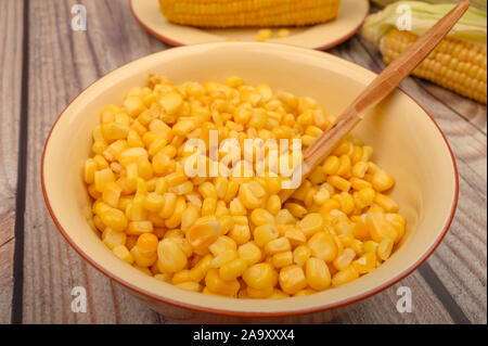 Grains de maïs doux dans une assiette avec une cuillère de bois et d'épis de maïs sur la table. Régime alimentaire sain. Régime alimentaire de remise en forme. Pour une petite douceur. Close up Banque D'Images