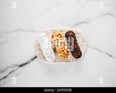 Ensemble de trois des éclairs sur fond de marbre. Vue rapprochée de la santé délicieux profitroles avec différents éléments de décor - chocolat, arachides et noix de coco. sherdded La verticale. Banque D'Images