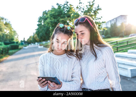 Deux filles ecolières petite amie 12-15 ans, regardant la vidéo phone, summer city après les cours l'école et le collège, l'automne pulls chauds. Casual Banque D'Images