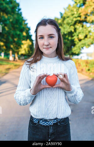 Adolescent teen girl holding a toy coeur rouge dans ses mains, l'été en ville, journée d'automne. Donner la vie et d'amour gratuit. Et comme le don de sang, de l'aide Banque D'Images