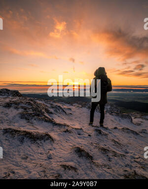 Randonneur debout sur un sommet des montagnes rocheuses à regarder la lumière dorée du soleil levant à l'aube sur un paysage d'hiver Banque D'Images