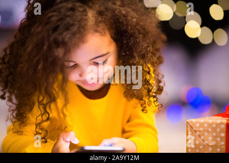 Jolie petite fille africaine jouant avec téléphone cellulaire à la veille de Noël Banque D'Images