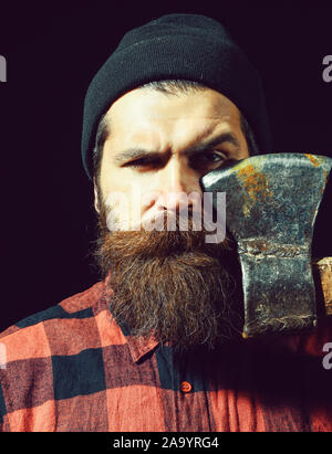 Bel homme ou bûcheron, hipster barbu avec barbe et moustache en hat détient old rusty lame de fer d'ax isolé sur fond noir Banque D'Images