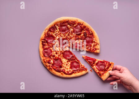 Prendre une pizza slice. La femme d'attraper un morceau de salami pizza sur fond violet. Voir ci-dessus de pizza au pepperoni. Dîner traditionnel italien Banque D'Images