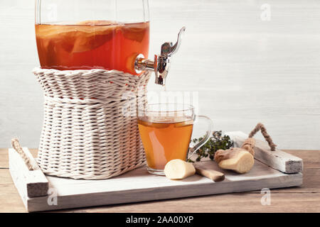 Des kombucha fermenté verre dans un pot avec robinet et dans une tasse sur un plateau blanc sur un fond de bois, copyspace. Banque D'Images