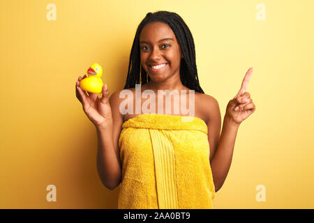 African woman holding serviette de douche canard sur fond jaune isolé très heureux pointant avec la main et le doigt sur le côté Banque D'Images