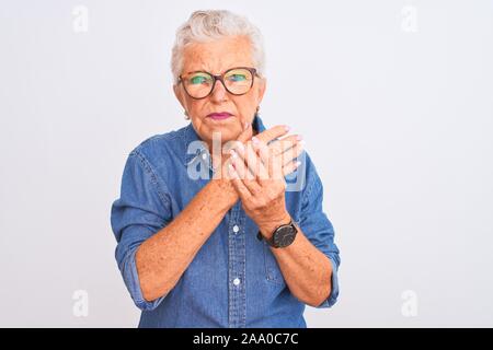 Aux cheveux gris Senior woman wearing denim shirt et lunettes sur fond blanc isolées souffrant de douleur sur les mains et les doigts, l'inflammation de l'arthrite Banque D'Images