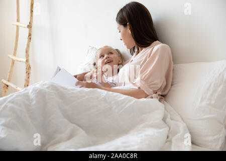 Famille heureuse de deux relaxing in bed, reading book. Banque D'Images