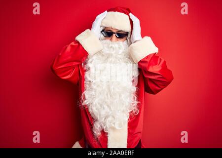 L'âge moyen homme portant un costume de Père Noël et des lunettes de soleil sur fond rouge isolés souffrant de maux désespérés et stressé car la douleur et Banque D'Images