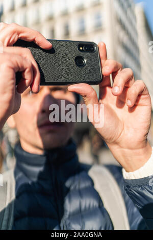 Jeune homme dans un PAC est de prendre une photo avec son téléphone portable dans la rue de ville européenne. Banque D'Images