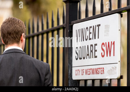 Un homme marchant avec la clôture en métal avec un panneau de rue qui entoure le terrain de jeu et le terrain de sport à Vincent Square City de Westminster, Londres. Banque D'Images