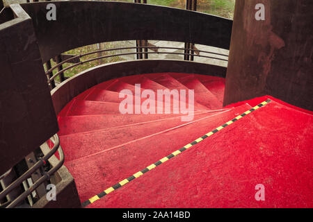 Cylindrique en acier rouge vif / escalier en spirale / escalier avec une rampe en acier brun massif et cylindre central dans un parking chambre Banque D'Images