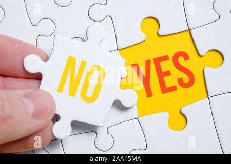 La notion de changement de position de Non à Oui. Une pièce du puzzle est tenu par un homme avec ses doigts sur un fond jaune. Close up. Banque D'Images
