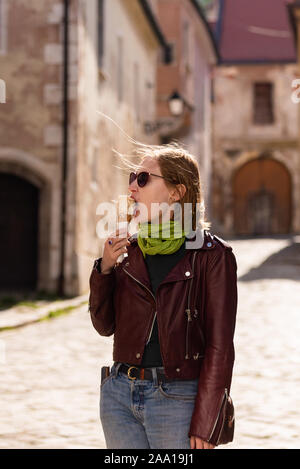 Fille et la crème glacée. Promenade dans Bratislava. Veste en cuir et des lunettes de soleil. Soleil dans ses cheveux et un foulard vert. Sur l'ancienne rue. Banque D'Images