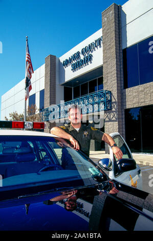 Une Orange County, CA, adjoint du shérif pose avec sa voiture de patrouille à l'extérieur d'un ministère en poste de shérif Aliso Viejo, CA. Banque D'Images