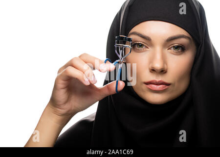 Jeune femme musulmane en hijab using eyelash curler isolated on white Banque D'Images