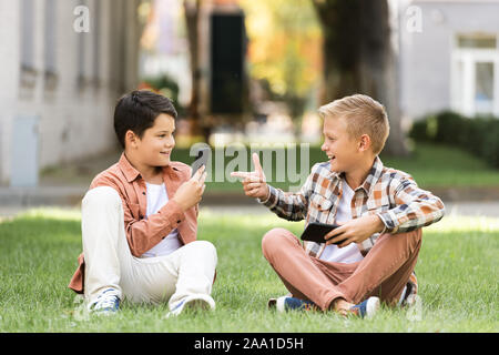 Garçon joyeux pointant du doigt avec smiling brother assis ensemble sur la pelouse Banque D'Images