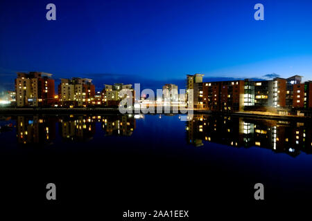 Les quais et le port de plaisance de Swansea au crépuscule à la recherche à travers l'eau d'une tour éclairée de blocs d'appartements à réfléchir sur la surface de l'eau encore Banque D'Images